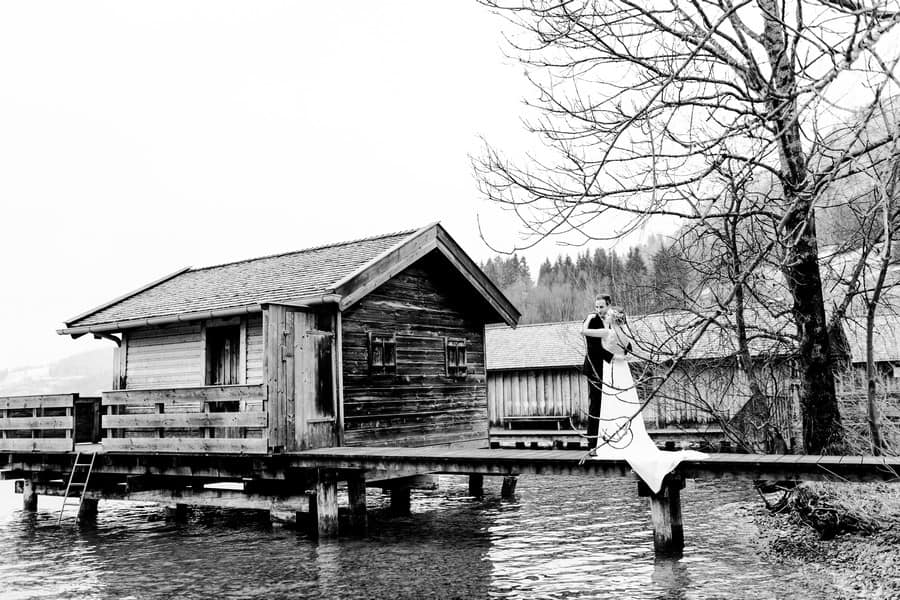Ein Brautpaar-Shooting mit Boho-Vintage-Brautkleid mit Schleppe und Spitze auf dem Steg am Schliersee